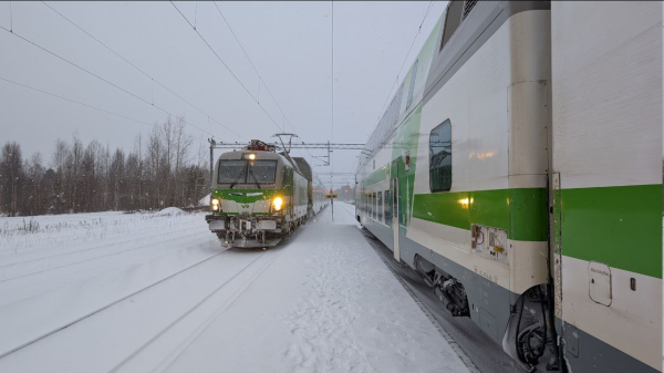 A narrow platform in the middle, a green VR Vectron pulls an Intercity train to the front of the picture on the left, a double-decker VR Intercity train on the right, snow covers the platforms and the tracks