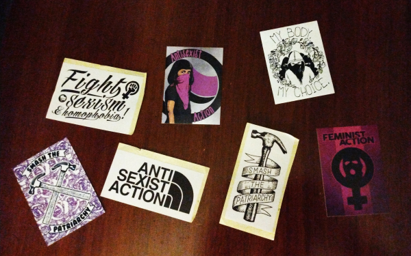 Seven stickers on a wooden table.
1. Fight sexism & homophobia!
2. Antifascist Action (showing a woman with a pink bandana)
3. My Body My Choice (showing a woman wearing black bandana)
4. Smash the Patriarchy (lavender background and two hammers crossed)
5. ANTI SEXIST ACTION
6. Smash the Patriarchy (showing a hammer with a ribbon wrapped around it)
7. Feminist Action (Pink and purple background, female symbol with a masked person in the center)