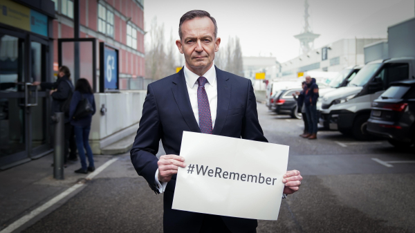 Volker Wissing hält ein Schild in den Händen, auf dem "#WeRemember" steht. Der Minister blickt ernst in die Kamera.