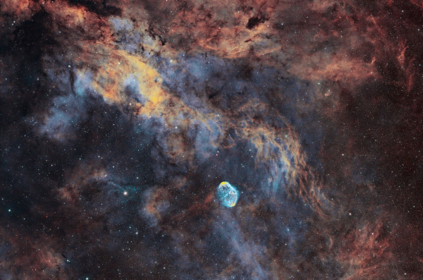 Astro photograph showing emission nebulae clouds in light blue, dark orange and gold.