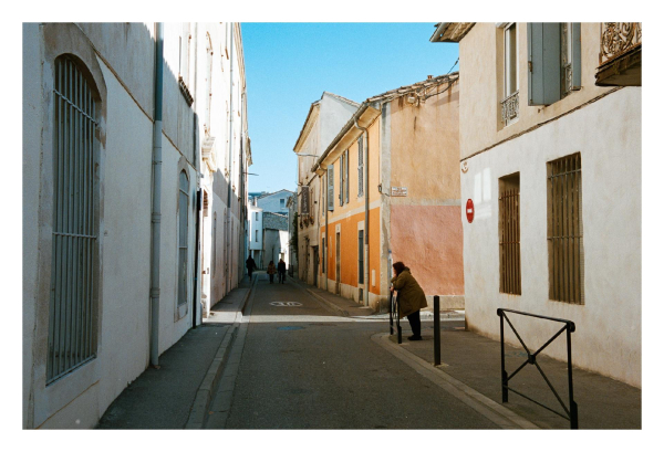 A woman standing in front of an orange house, bathed in light in an otherwise shadowed street.