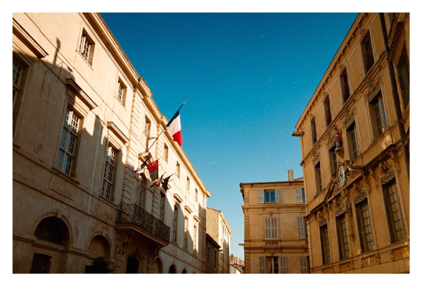 A french flag on a building divided by light and shadow. A blue sky.