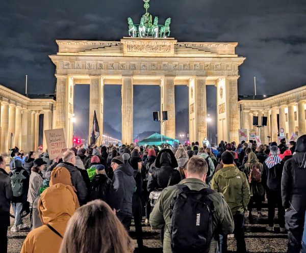 Vor dem erleuchteten Brandenburger Tor stehen viele Menschen.