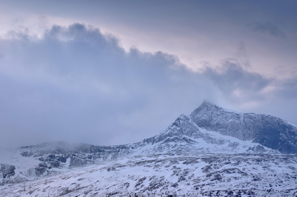 Polar night in the Narvik region. A glow in the sky behind the clouds bleed light into the snow dusted cliffs of yet another Norwegian mountain.