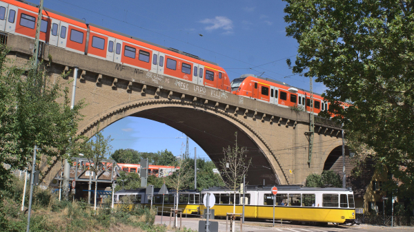 Die große Steinbogenbrücke der Gäubahn/Panoramabahn über die Nordbahnhofstraße auf der eine S-Bahn fährt. Im Hintergrund eine unter den Bogen ist eine S-Bahn vom Nordbahnhof auf einer kleineren Stahlbrücke zu sehen. Unter der Gäubahnbrücke fährt eine Museumsstraßenbahn.