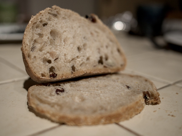 Pain noisette amande raisin bio, une tranche sur la table (à carreaux beige), le reste du pain posé dessus, légèrement incliné vers l'arrière.