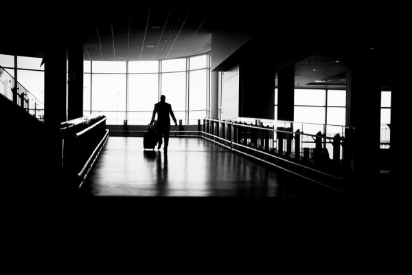 The silhouette of a traveler walking down a wide ramp. He's framed within the light of large windows in the background. Vancouver 2007