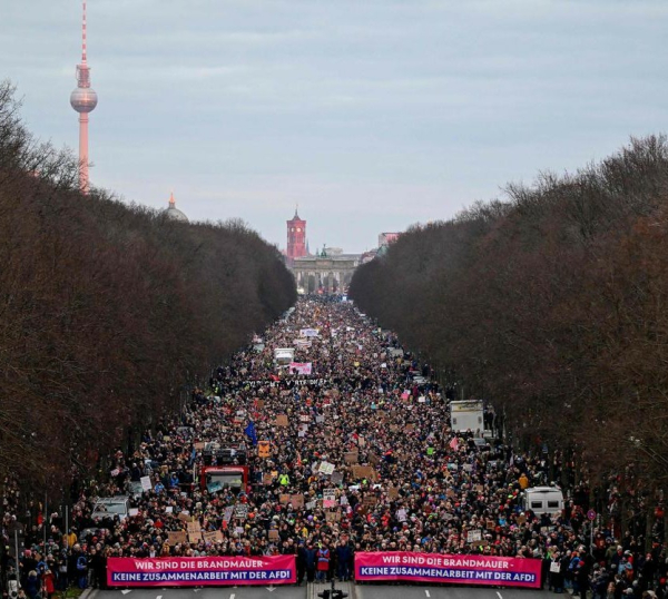 The broad avenue leading to the Brandenburg Gate from the West is tightly packed with demonstrators as far as the eye can see. A small Brandenburg Gate is far in the background, as are Berlin's Town Hall and, to the side, its landmark TV tower.