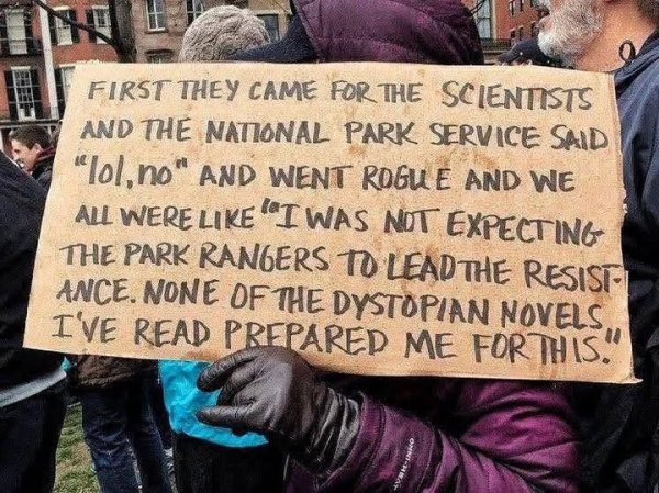 A cardboard poster held by an unknown person reads: First they came for the scientists and the National Park Service said "LOL, no" and went rogue and we all were like "I was not expecting the Park Rangers to lead the resistance. None of the Dystopian novels I've read prepared me for this."