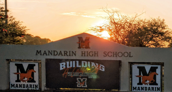 Golden sky above an ornate ground sign for the Mandarin High School. With logos for the mascot, Mandarin Mustangs.