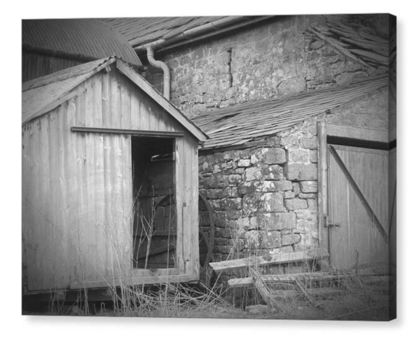 Black and white photograph as a canvas.  The image shows a dilapidated wooden shed by an old farm building.  Contents unknown.