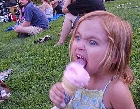 young girl with blue eyes and red hair eating an ice cream cone with a maniacal look on her face