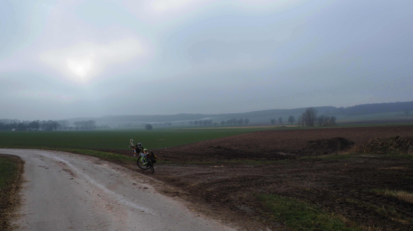 Fahrrad an einem Acker, eine fahle Sonne am Himmel