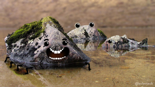 A photo of 3 boulders in the shallow edge of a Scottish loch, against the backdrop of a blurred brown mountainside. The largest rock is on the left in the foreground. It has a lot of green moss across the top, and a face with a big toothy smile drawn on, and multiple little legs supporting it under the water. The other two rocks are smaller, and further away. One has been edited to have two frog-like eyes sticking up on top, the other on its right has been tweaked to emphasise its fish-like profile shape, and has a single eye drawn on. Both are covered with lichen and moss.