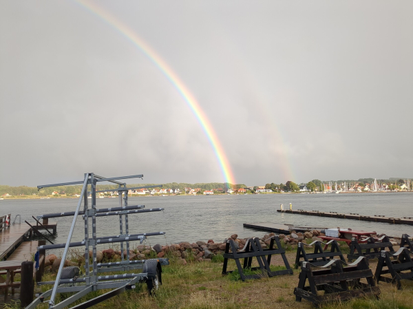 Rainbow ending in the gray blue water of the harbour. Boats on the edge of the view.