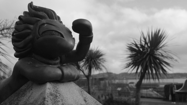 Lemming statue on top of an obelisk peering ahead. Palm trees in the background.