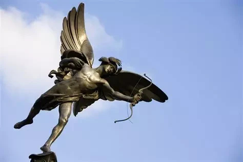 Photo of a winged Cupid sculpture with a bow in hand against a blue sky.