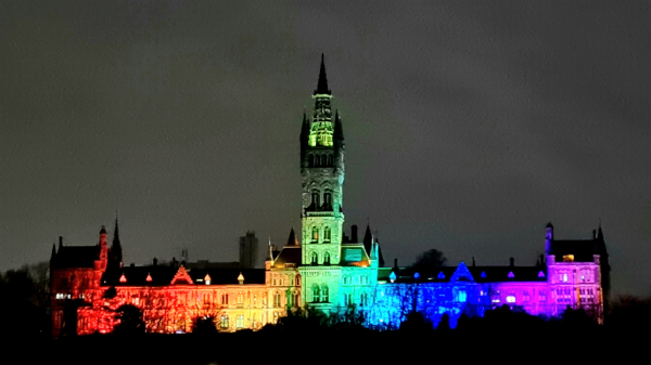 The Gothic main building and tower of Glasgow university lit up with rainbow-coloured lights.