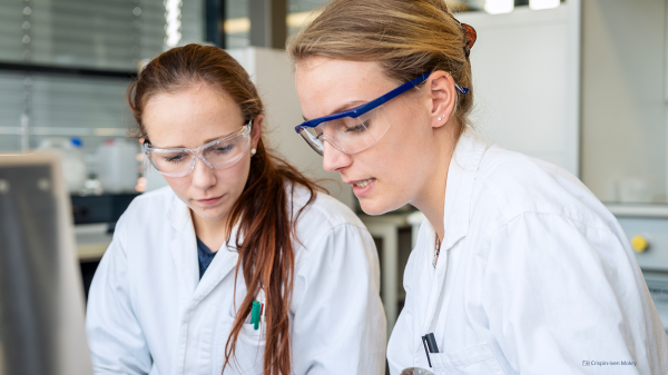 Foto von zwei Frauen im Labor. Beide tragen Arbeitskleidung und Schutzbrillen.