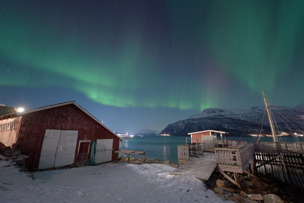 The old boat shed and jetty at Elvegård, to the north of Grov. Street lights illuminate the foreground, with auroras illuminating the sky.