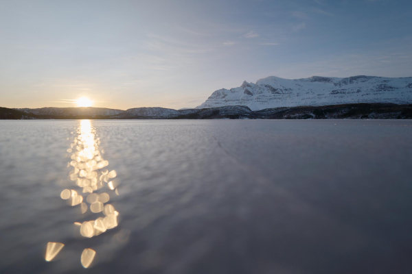 Sunlight glistens over the ice on the surface of a frozen lake. 