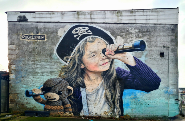 A mural of a young girl and her teddy bear playing at priates.