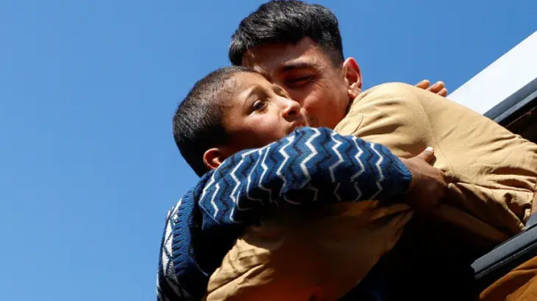 A man hugging a boy against the background of blue sky.