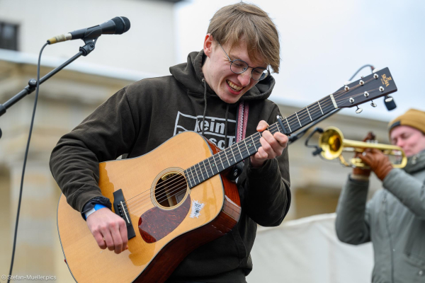 Marlo Grosshardt spielt beim Klimastreik von Fridays for Future Gitarre. Rechts Hannes Koch mit Trompete. Brandenburrger Tor, Berlin, 14.02.2025