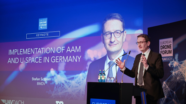 Staatssekretär Stefan Schnorr steht vor einem Rednerpult und gestikuliert, um seinen Worten Ausdruck zu verleihen. Er hält eine Keynote auf dem European Drone Forum, was durch eine Präsentation im Hintergrund deutlich wird. Der Titel lautet: "Implementation of AAM and U-Space in Germany".