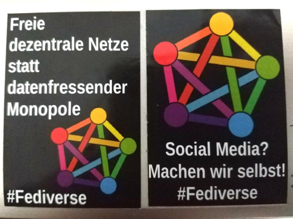 Zwei schwarze Sticker mit regenbogen-bunten Fediverselogo, ein 5-knotiges Peer-Netzwerk, bei dem alle Knoten gleichmäßig verteilt und miteinander verbunden sind.

Auf dem linken Sticker ist außerdem in weiß zu lesen: "Freie dezentrale Netze statt datenfressender Monopole #Fediverse".

Auf dem rechten stehtv " Social Media? Machen wir selbst! #Fediverse".