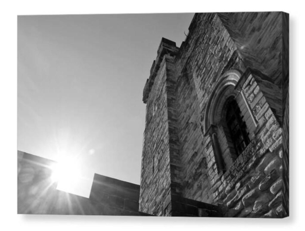 Black and white photograph shown as a canvas print.  To the right the tall tower of a castle, to the left the sun glares over the battlements.