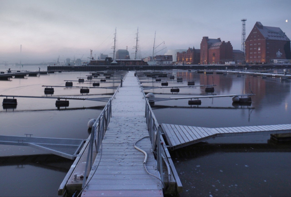 The view leads into the picture on a hooped jetty. The harbor lies on the horizon in the morning mist.