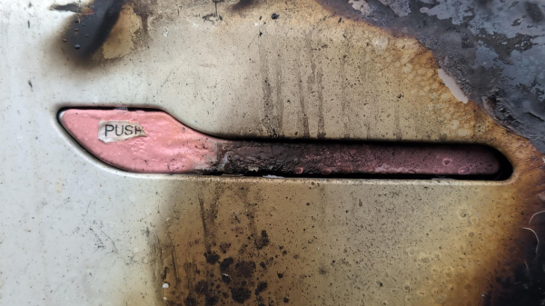 The handle of a white Tesla with pink accents after a car fire. The handle has a small label printed on it that says "PUSH", which is still semi-intact.