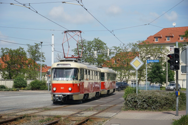 Zwei vierachsige Hochflur-Straßenbahnwagen mit relativ runder Kopfform befahren eine zweigleisige Strecke, die vom Verlauf in der Fahrbahn zu Schottergleis übergeht. Die Wagen sind beige mit roter Bauchbinde lackiert.