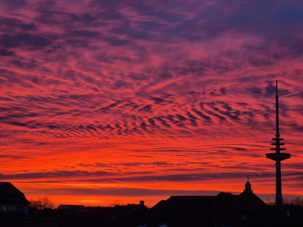 Morgendämmerung in Bremen. Vor einem Himmel in leuchtendem orange, rot und lila ist der Bremer Fernsehturm zu sehen.