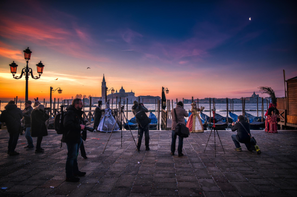 Kostümierte Personen werden in der Morgendämmerung in Venedig von Fotografen belagert.