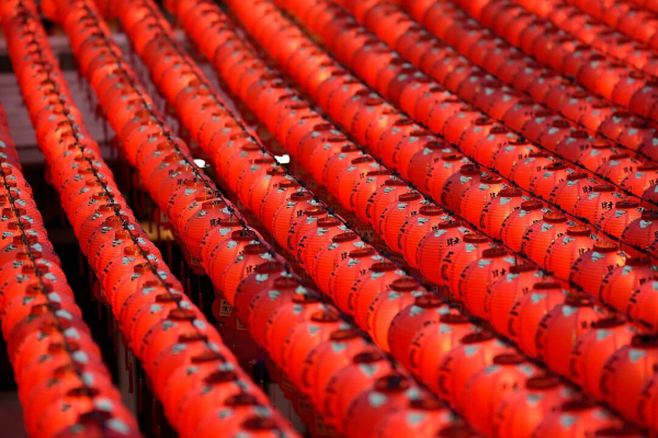 This image features rows of vibrant red lanterns adorned with black calligraphy, creating a mesmerizing pattern. The repetition of the lanterns and the shallow depth of field give the image a sense of depth and rhythm. The warm glow and intricate details of the characters evoke a cultural atmosphere from a temple setting.