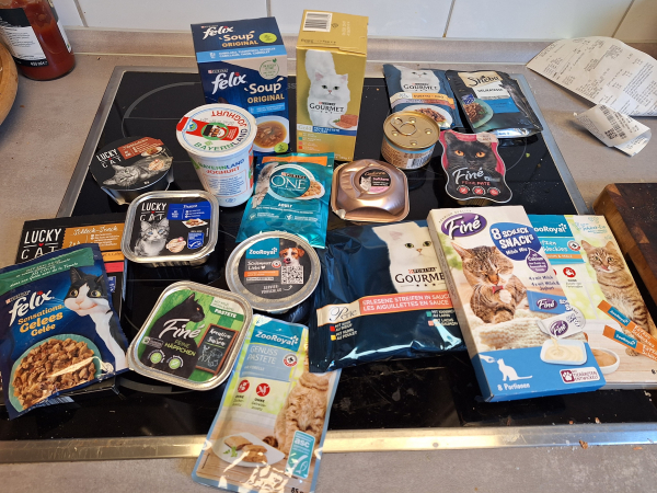 Nassfutter und Snacks für Katzen verschiedener Hersteller und verschiedenen Verpackungen sind auf einem Kochfeld ausgebreitet. 

Marken sind: Finé, Felix, ZooRoyal, Lucky Cat, Purina, Sheba. 

Es scheint eine Portion Nassfutter für Hunde dabei zu sein.