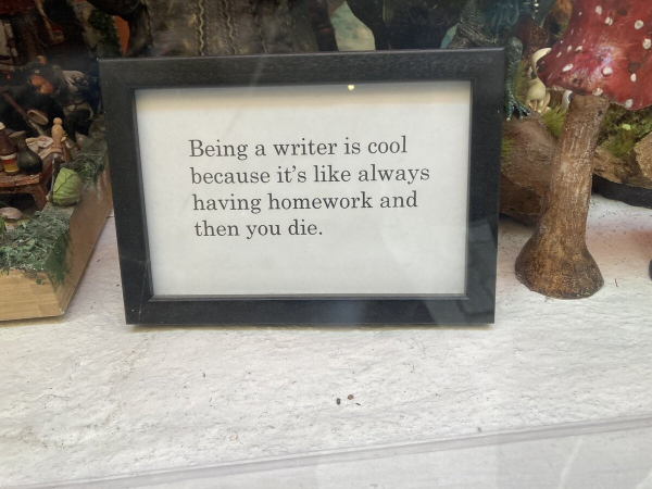 Little sign on a table next to a ceramic mushroom that says: "Being a writer is cool because it's like always having homework and then you die."