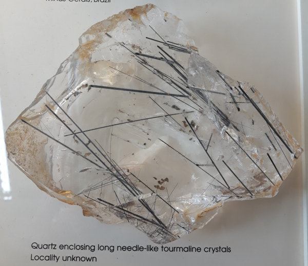 A lump of colourless and transparent quartz filled with black needles of tourmaline. Label text: Quartz enclosing long needle-like tourmaline crystals. Locality unknown.