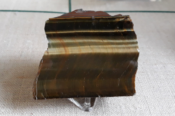 A brown polished slab of tiger's eye showing an optical effect called chatoyancy, where there are bands of gold which appear to glow.