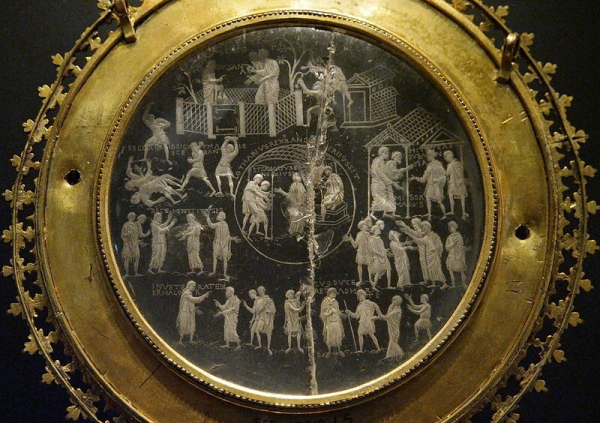 A circular piece of colourless quartz mounted in an ornate golden frame. There are several scenes carved into the quartz showing people interacting with each other.