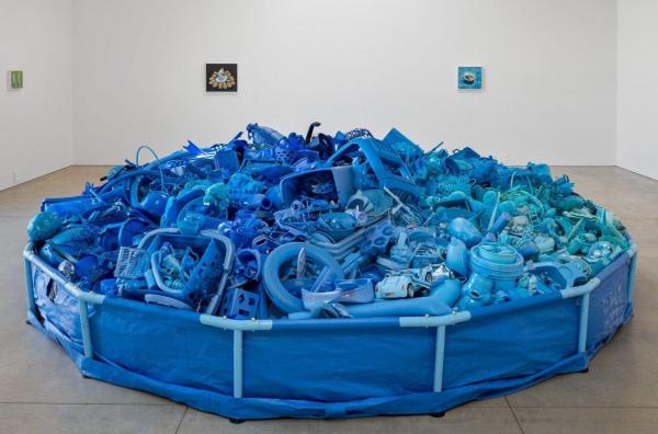 Large found object sculpture of a blue above-ground round pool filled high with an assortment of blue plastic objects.