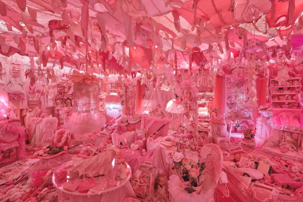 Room-size installation of a domestic space filled with entirely pink objects lining the floor, walls, and ceiling, mostly soft fabrics, feminine ephemera, and bedroom furniture.