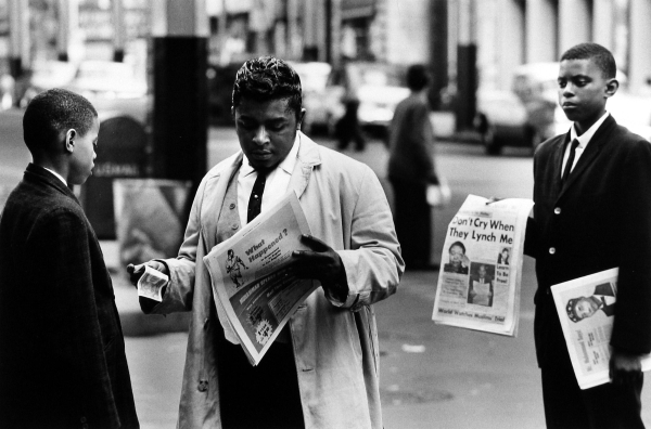 Black and white photo of a Black man in a light coat buying a newspaper from a young Black boy in a suit, as another Black boy holds out a newspaper with a headline reading "Don't Cry When They Lynch Me".