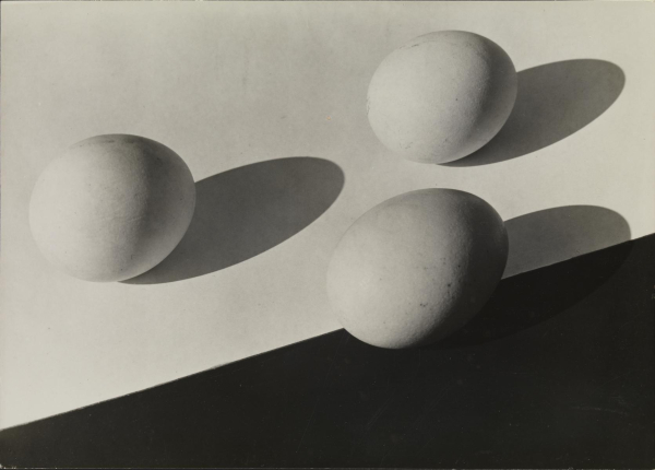 Black and white photo of three eggs on a black and white table, with shadows falling across the surface.