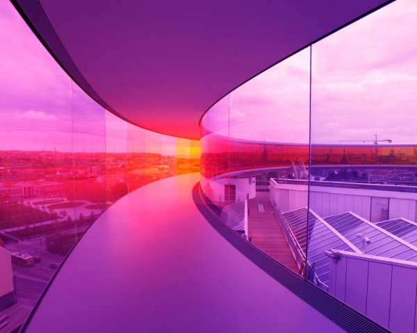 A curving hallway with floor-to-ceiling window walls revealing an urban landscape, lit in a purple and orange glow.