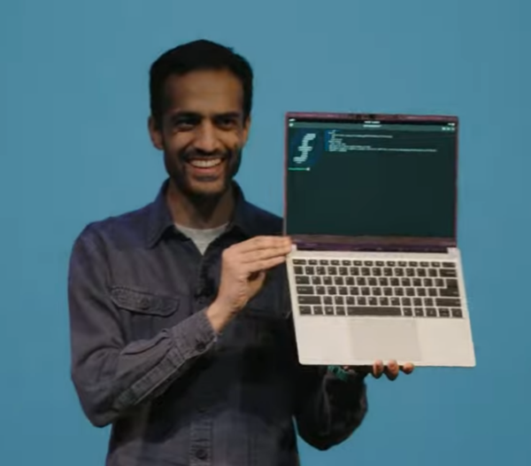 Framework CEO Nirav Patel smiling while holding a Framework Laptop 13 with Fedora Linux installed.