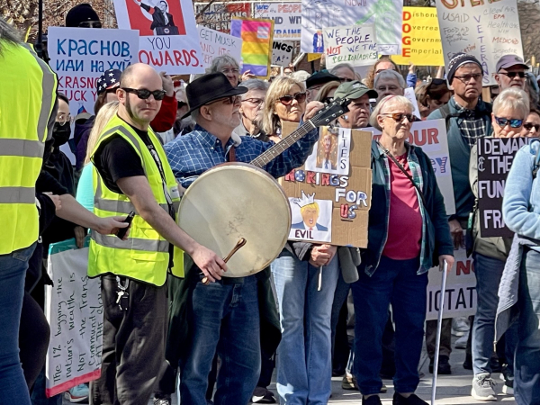 Crowd of protesters with placards.  One man has a guitar and another has a drum.