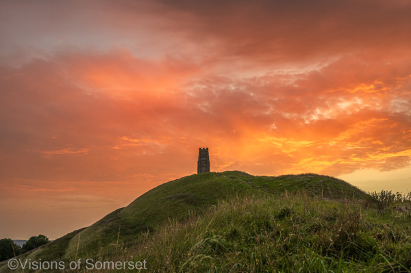 Bright red sky above the tower and hill. 